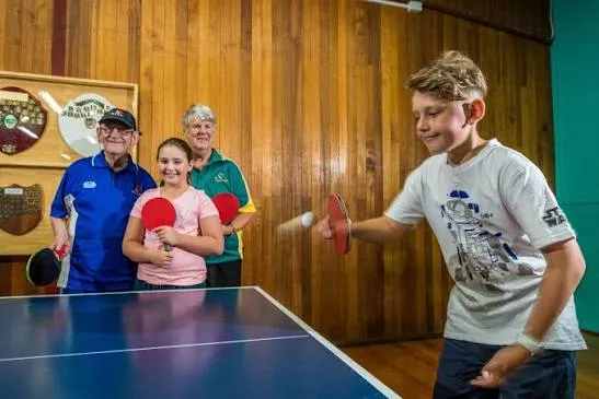 A junior player mid-shot while senior club members watch on at the Devonport clubrooms